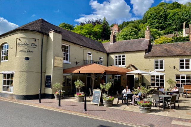 The front view of the White Hart Inn in Ironbridge Telford. There is outdoor seating in the courtyard with large umbrellas and outdoor heating